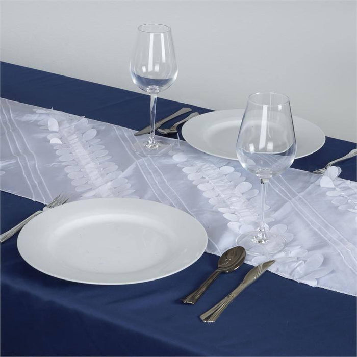 Elegant white table runner on a navy tablecloth with plates and glasses.