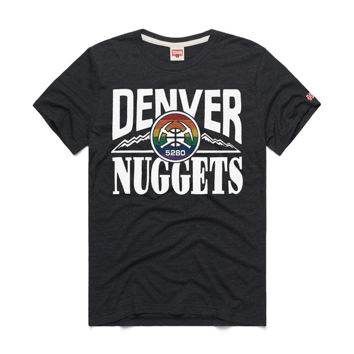 black short-sleeve crewneck t-shirt displaying a large retro Denver Nuggets graphic on the chest. The word 'DENVER' arcs across the top and 'NUGGETS' sits straight below in bold white lettering. Centered between the words is a circular team logo with crossed white pickaxes and a basketball, set against a vibrant rainbow-striped backdrop. A stylized jagged mountain line extends horizontally from behind the circular emblem, and a tiny orange brand logo is visible on the left sleeve hem