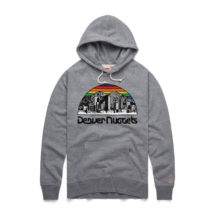 A heather gray pullover hoody featuring a retro Denver Nuggets graphic on the center chest. The design showcases a black-and-white sketch of a city skyline and mountain range contained within a semi-circle dome. The top curve of the dome is filled with a vibrant orange, yellow, and green sunset-striped gradient. Underneath the graphic, the team name 'Denver Nuggets' is printed in a black, stylized 1970s bubble font. The hoody includes cream-colored drawstrings, a front kangaroo pocket, and a sma