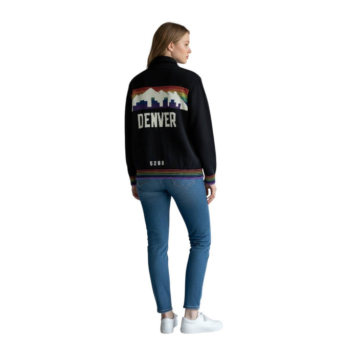 Full-body studio back view of a female model wearing a black button-up cardigan sweater, light-wash blue jeans, and white sneakers against a white background. The back of the cardigan features a large retro design across the shoulders showing a white mountain skyline over horizontal rainbow stripes. Below the graphic, 'DENVER' is printed in bold white block letters, with a small white 'NUGGETS' text logo near the rainbow-trimmed waistband.