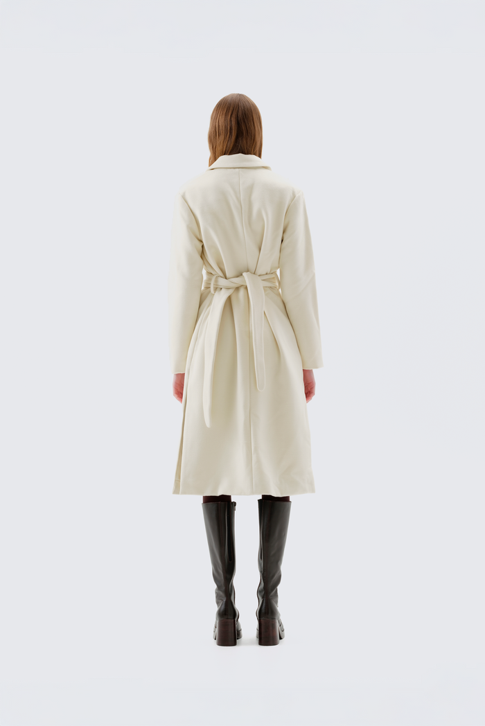 Cream faux wool coat with notch lapel, self-belt at the waist, and raw-edge trim, worn full-length over black boots, back view