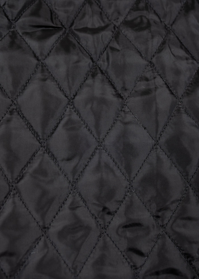 Close-up of black quilted fabric with diamond stitching pattern, creating a textured and elegant appearance.