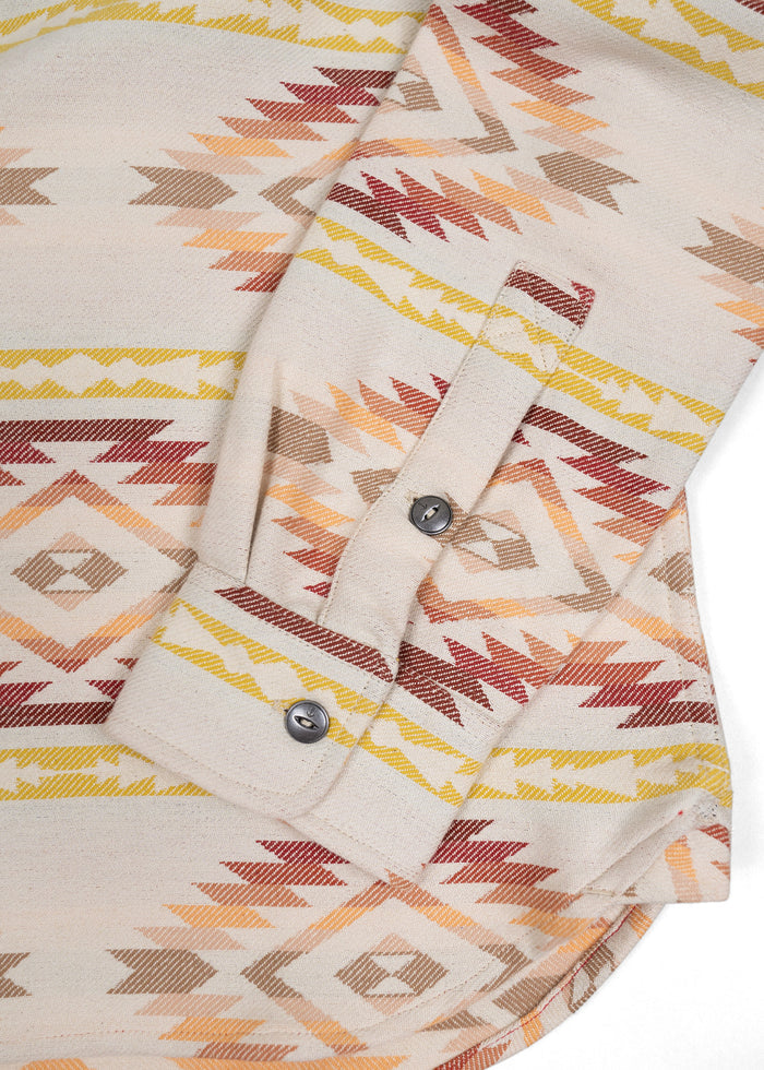 Close-up of a beige shirt with colorful geometric patterns and buttoned cuffs, showcasing intricate design details.