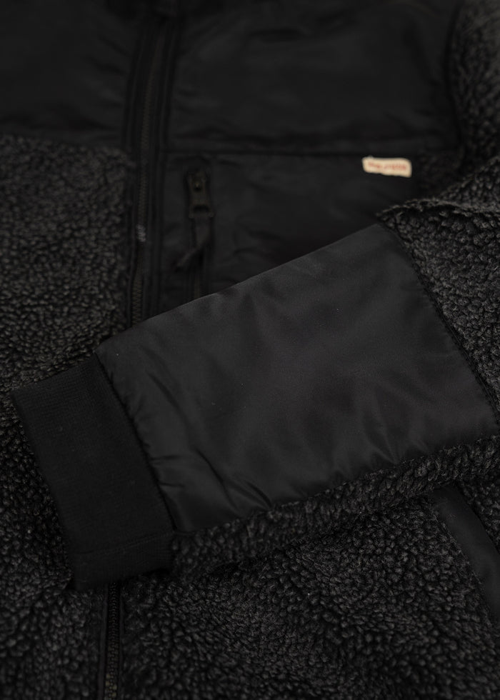 Close-up of a black sherpa fleece jacket with a nylon sleeve and zipper, highlighting texture and detail.