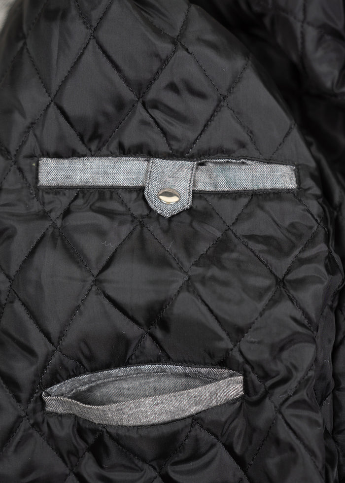 Quilted black fabric with a buttoned strap and open pocket, showcasing detailed stitching and texture.
