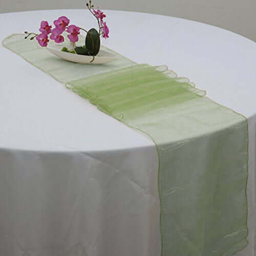 Green table runner on a white table with decorative flowers.