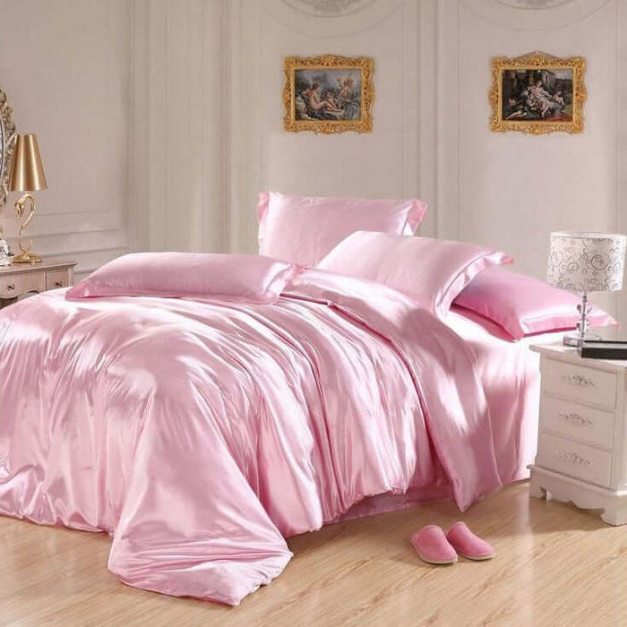 Pink satin bedding set with pillows and matching slippers in a styled bedroom.