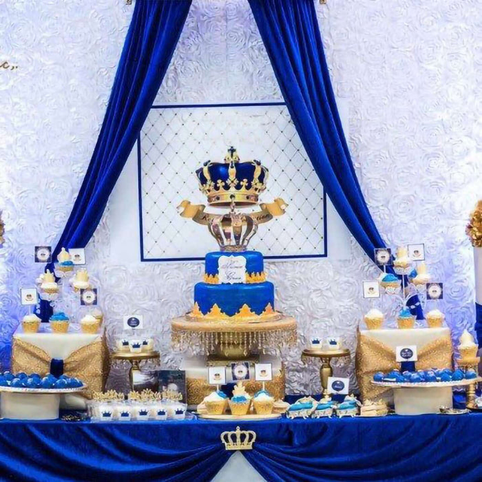 Elegant royal-themed dessert table with blue and gold cake and treats.