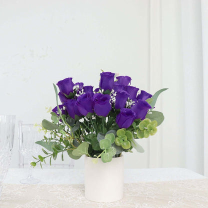 Purple rose bouquet in a white pot with greenery accents.