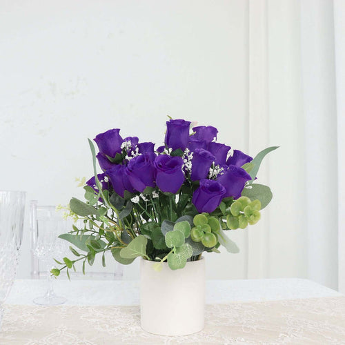 Purple rose bouquet in a white pot with greenery accents.