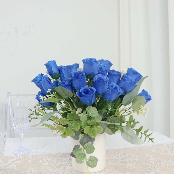 Blue roses arrangement in white vase with greenery accents.