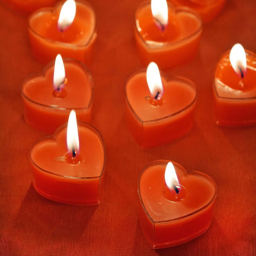 Heart-shaped orange candles with flames on a vibrant background.