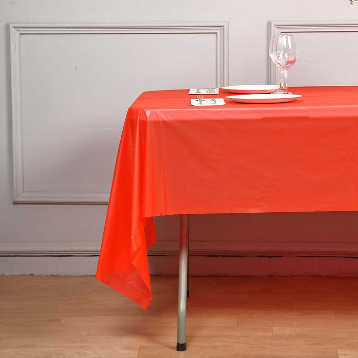 Red plastic tablecloth draped over a table set with plates and a wine glass.