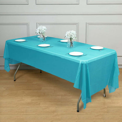 Turquoise tablecloth draped on a table set for dining with floral centerpieces.