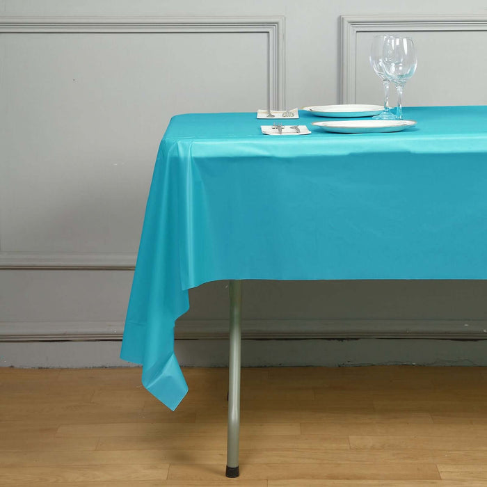 Turquoise tablecloth draped over a table with dinnerware and glassware.