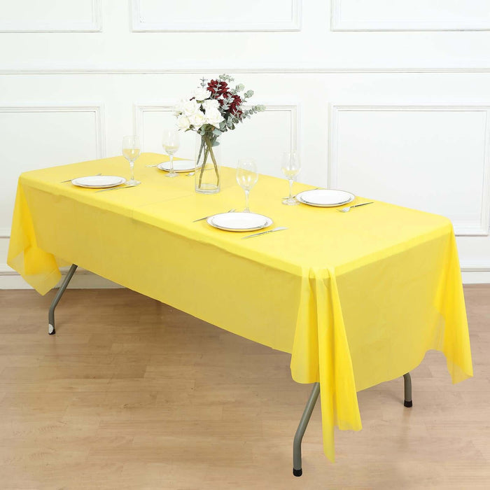 Yellow tablecloth draped over a table set for dining with plates and glasses.