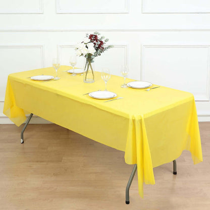 Yellow tablecloth draped over a table set for dining with plates and glasses.