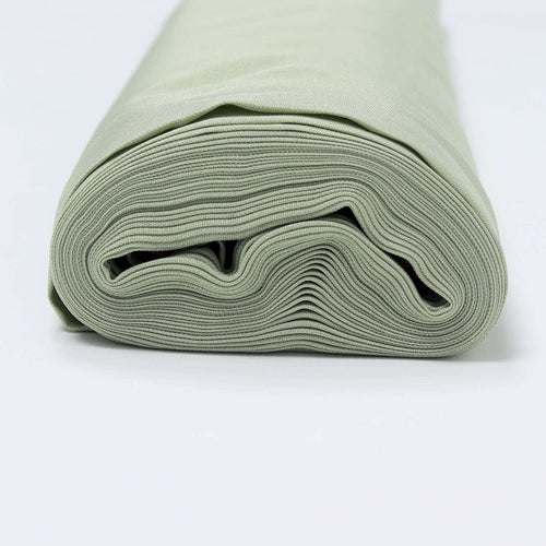 Rolled sage green fabric on a plain backdrop
