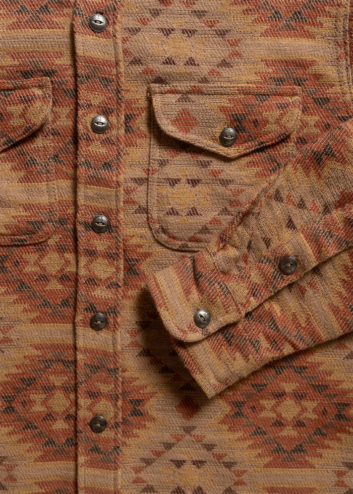 Close-up of a patterned brown and orange shirt with metal buttons and flap pockets, showcasing intricate geometric designs.