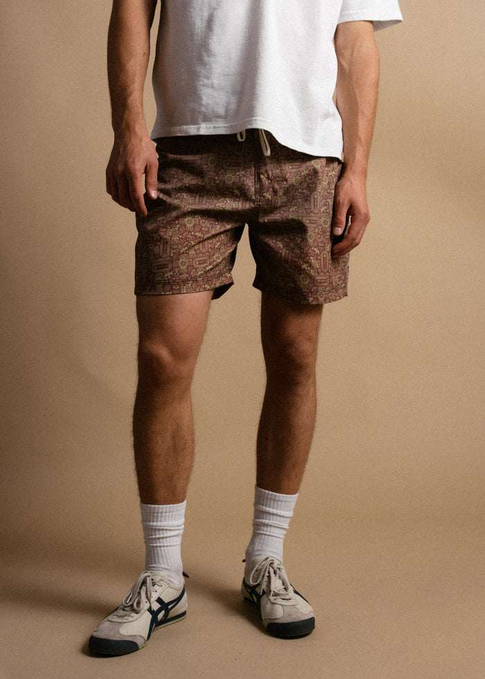Man in white shirt, patterned shorts, and sneakers stands on beige background, showcasing casual summer fashion style.