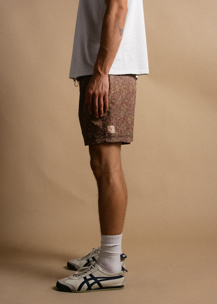 Man in white shirt, patterned shorts, and sneakers stands against a beige background, showcasing casual summer fashion.