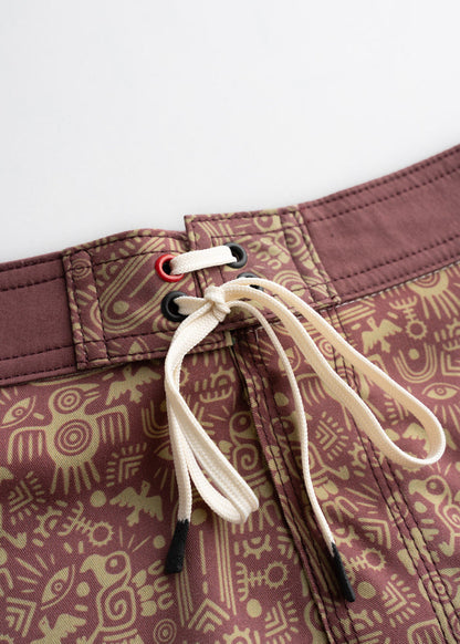 Close-up of brown shorts with tribal patterns and white drawstring, featuring red and black eyelets for a stylish look.
