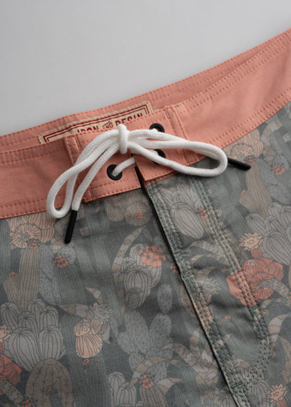 Close-up of swim trunks with a cactus pattern, featuring a peach waistband and white drawstring against a neutral background.