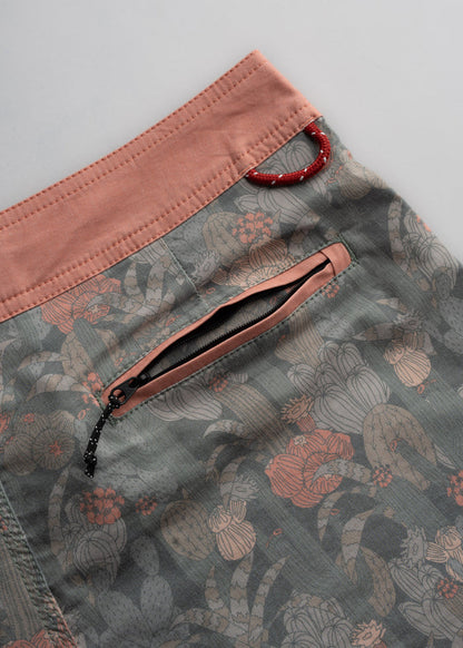 Close-up of floral-patterned shorts with a pink waistband, zipper pocket, and red loop detail on a light gray background.