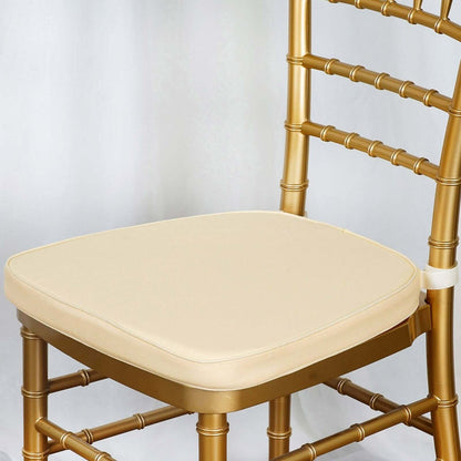 Gold chiavari chair with cream cushion on a plain backdrop.