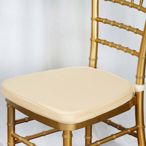 Gold chiavari chair with cream cushion on a plain backdrop.