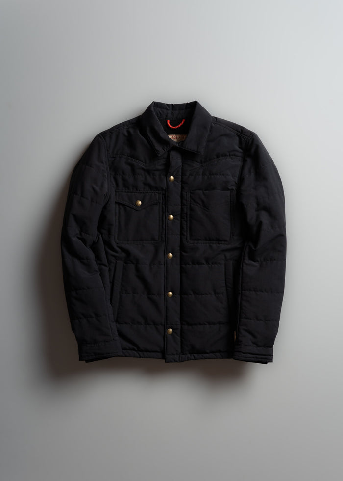 Black quilted jacket with gold buttons and chest pockets, displayed against a light gray background.