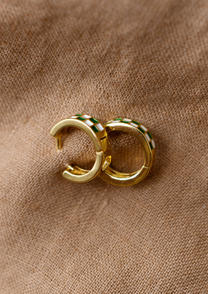 A pair of gold hoop earrings with green and white enamel checker pattern.