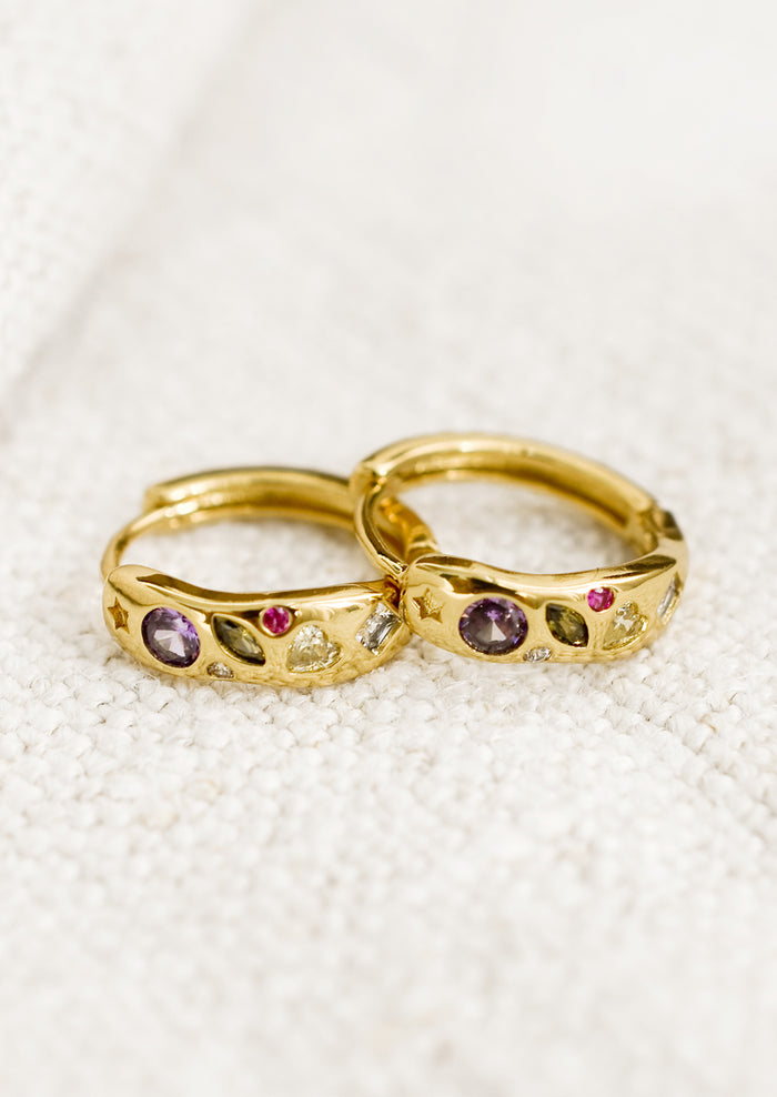A pair of gold huggie hoops with embedded crystals in a mix of colors and shapes.
