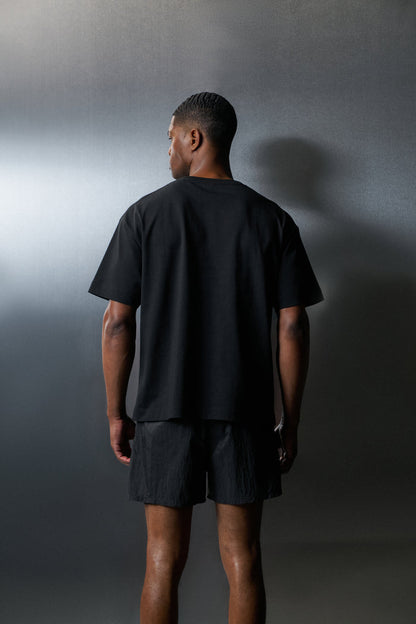 Person wearing a black t-shirt and shorts standing against a grey background