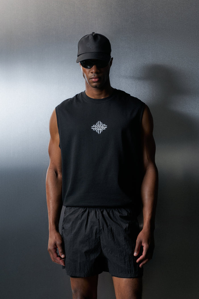 Man wearing a black sleeveless shirt and shorts with a logo, standing against a gradient grey background.
