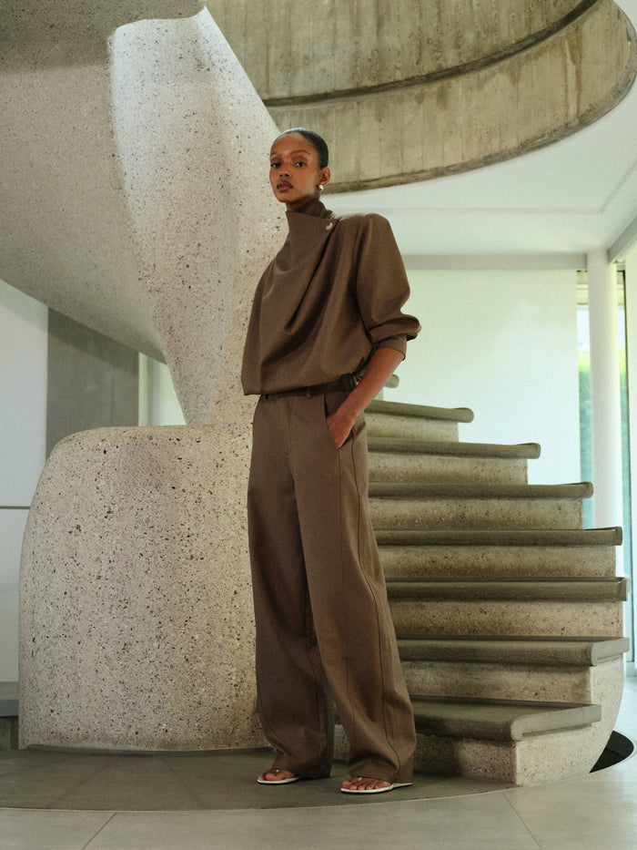 Person in a brown matching tailored set standing on a modern staircase.