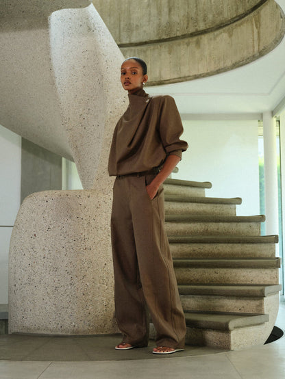 Person in a brown matching tailored set standing on a modern staircase.