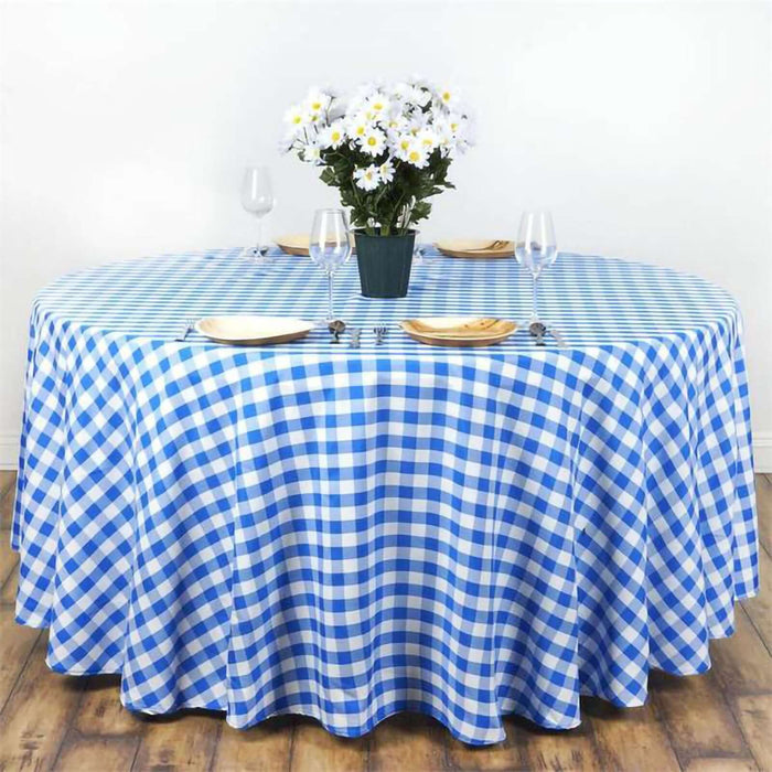 Blue and white checkered tablecloth draped over a round table with flowers and dinnerware.