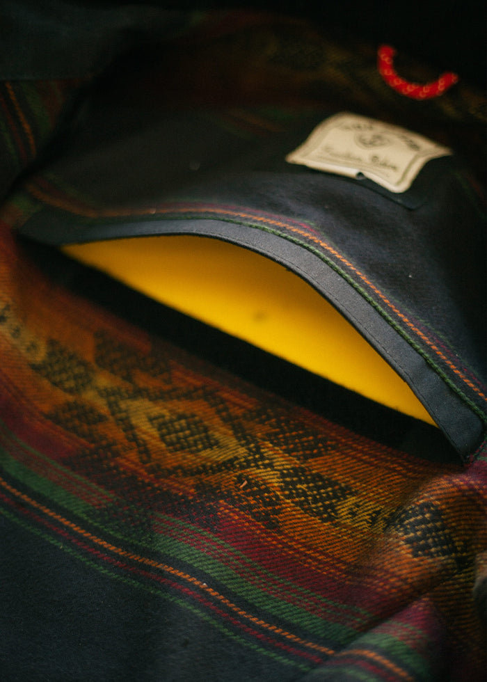 Wool jacket with colorful Aztec pattern, yellow lining, and label. Red loop visible. Close-up of fabric texture and design.