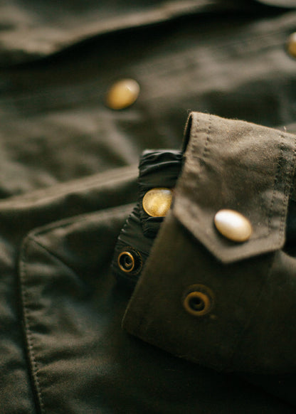 Close-up of a dark green jacket with brass buttons and grommets, highlighting the texture and design details.