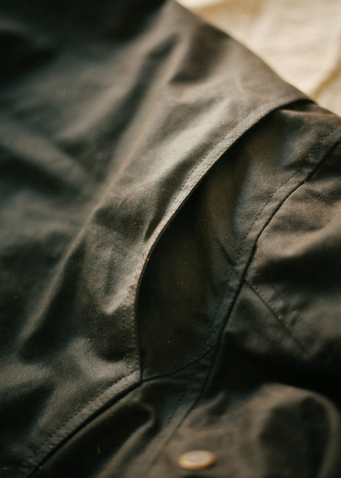 Close-up of a black jacket's shoulder seam, highlighting the fabric texture and stitching detail in soft lighting.