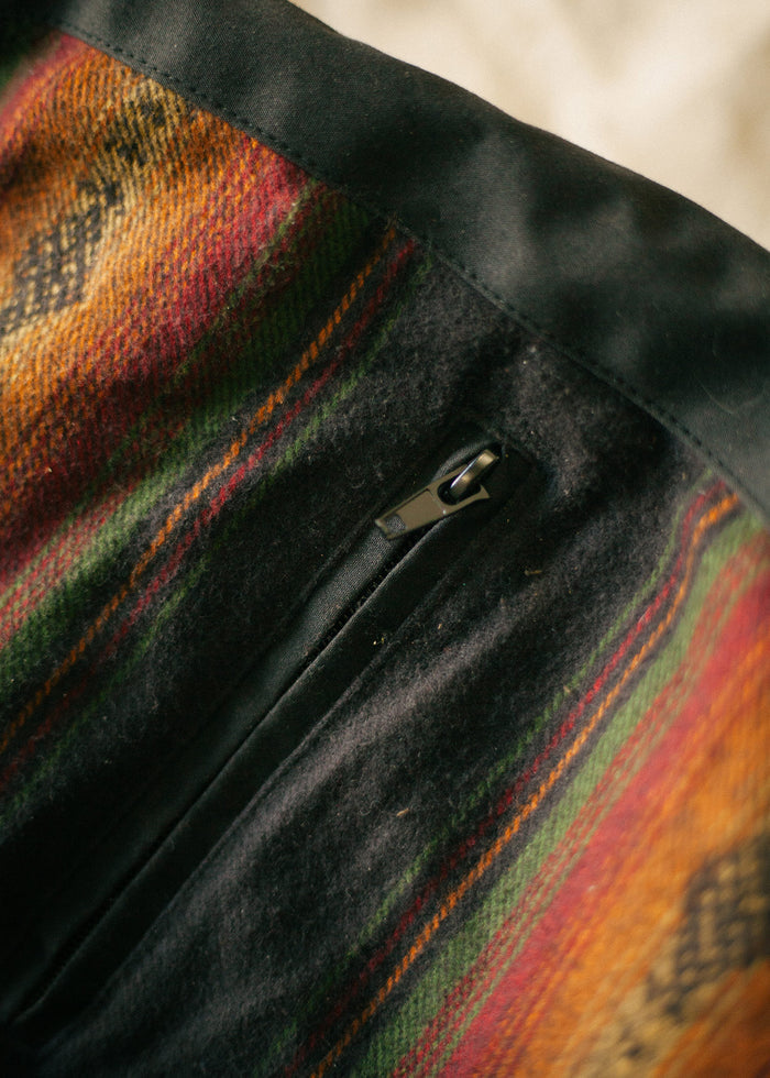 Close-up of a colorful woolen fabric with a black zipper, featuring vibrant stripes in red, green, and orange hues.