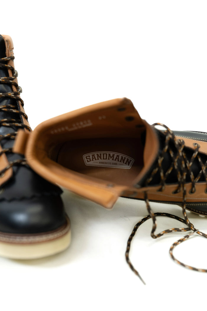 Black and tan boots with visible "Sandmann" logo inside, showcasing detailed laces and sturdy design on a white background.