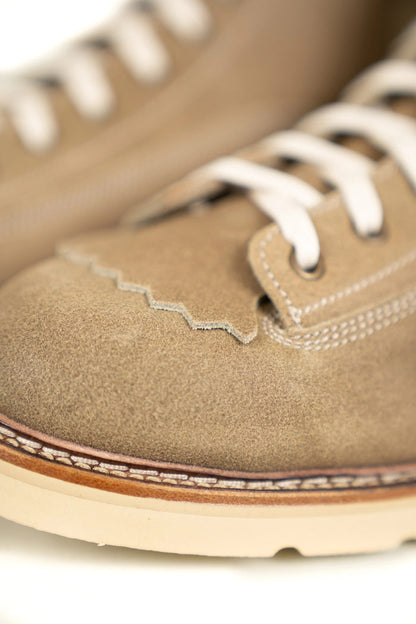 Close-up of tan suede shoes with white laces, highlighting detailed stitching and textured leather for a stylish look.