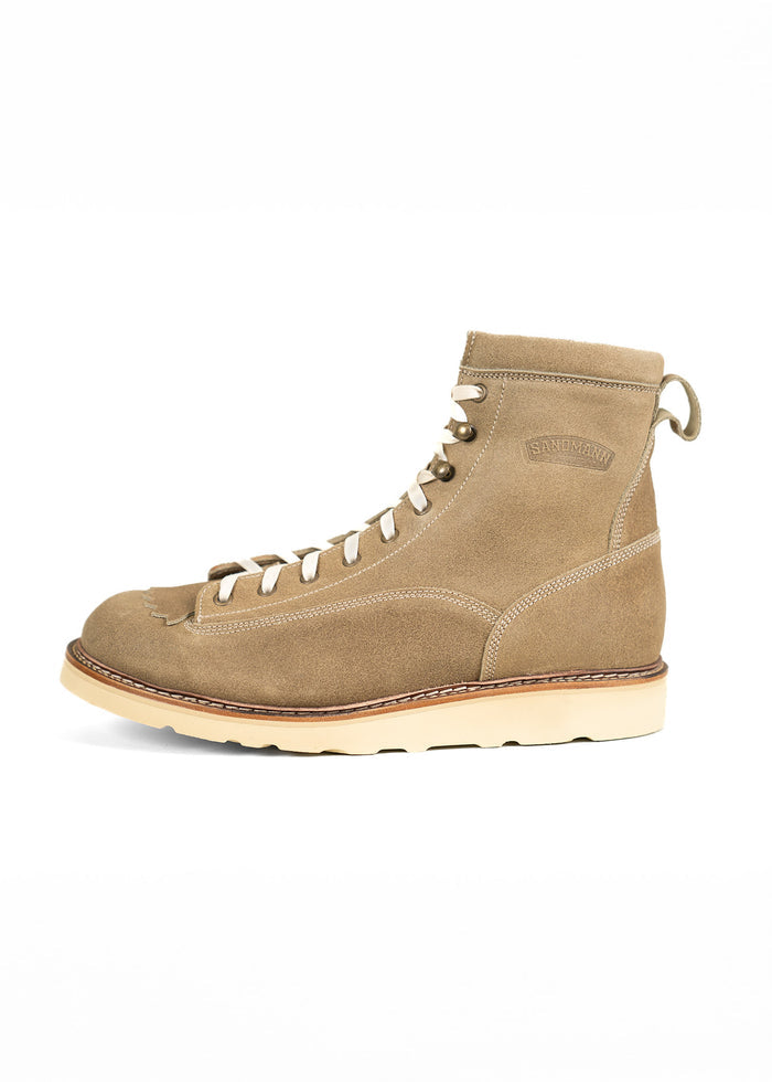 Tan suede boot with white laces and a beige sole, side view. Embossed logo on ankle. Simple, stylish design on white background.