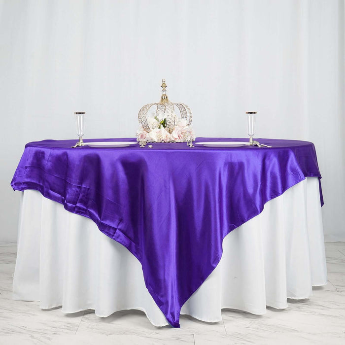 Purple satin tablecloth draped elegantly over a white table with decorative crown and candles.