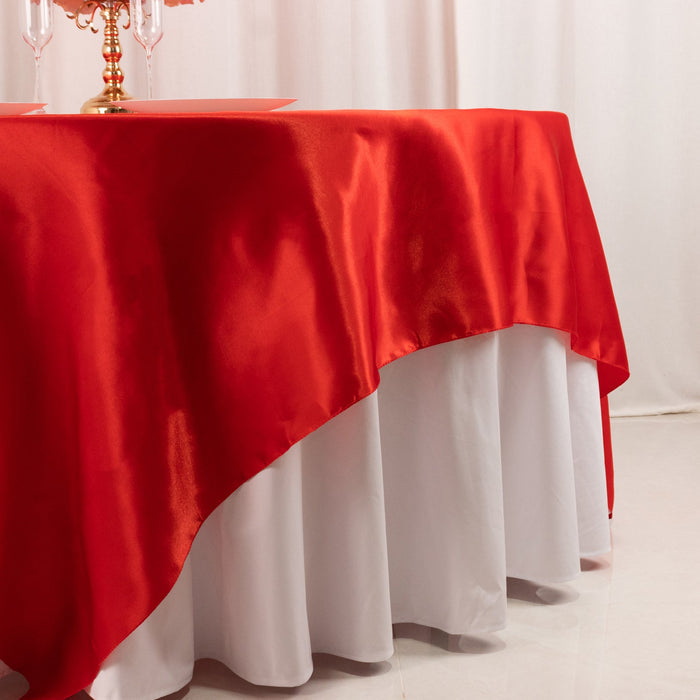 Red satin tablecloth draped over white table, elegant dining setup.