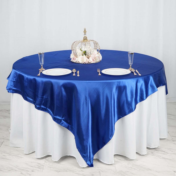 Elegant blue satin tablecloth draped over a round table with a crown centerpiece.