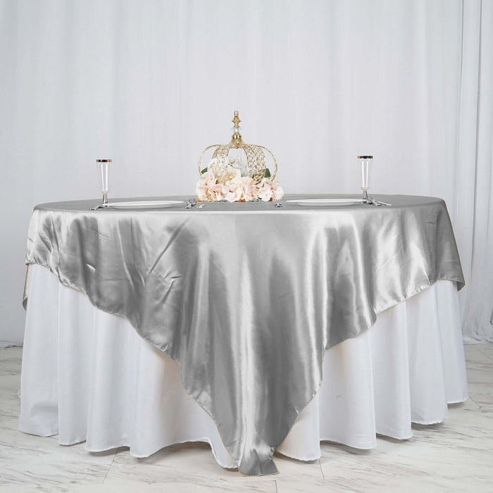 Elegant silver satin tablecloth draped over a round table with floral centerpiece.