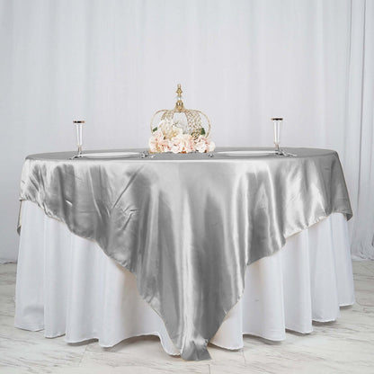 Elegant silver satin tablecloth draped over a round table with floral centerpiece.